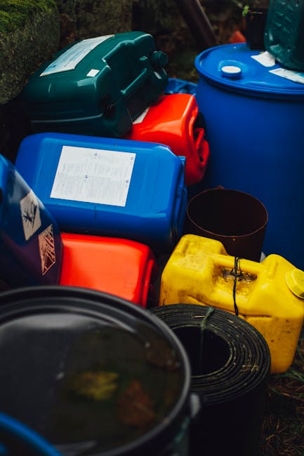 A red wheeled bin designated for clinical waste disposal, featuring a textured plastic surface with a hinged lid sitting in an outdoor urban environment on a concrete pavement. The bin displays a blac